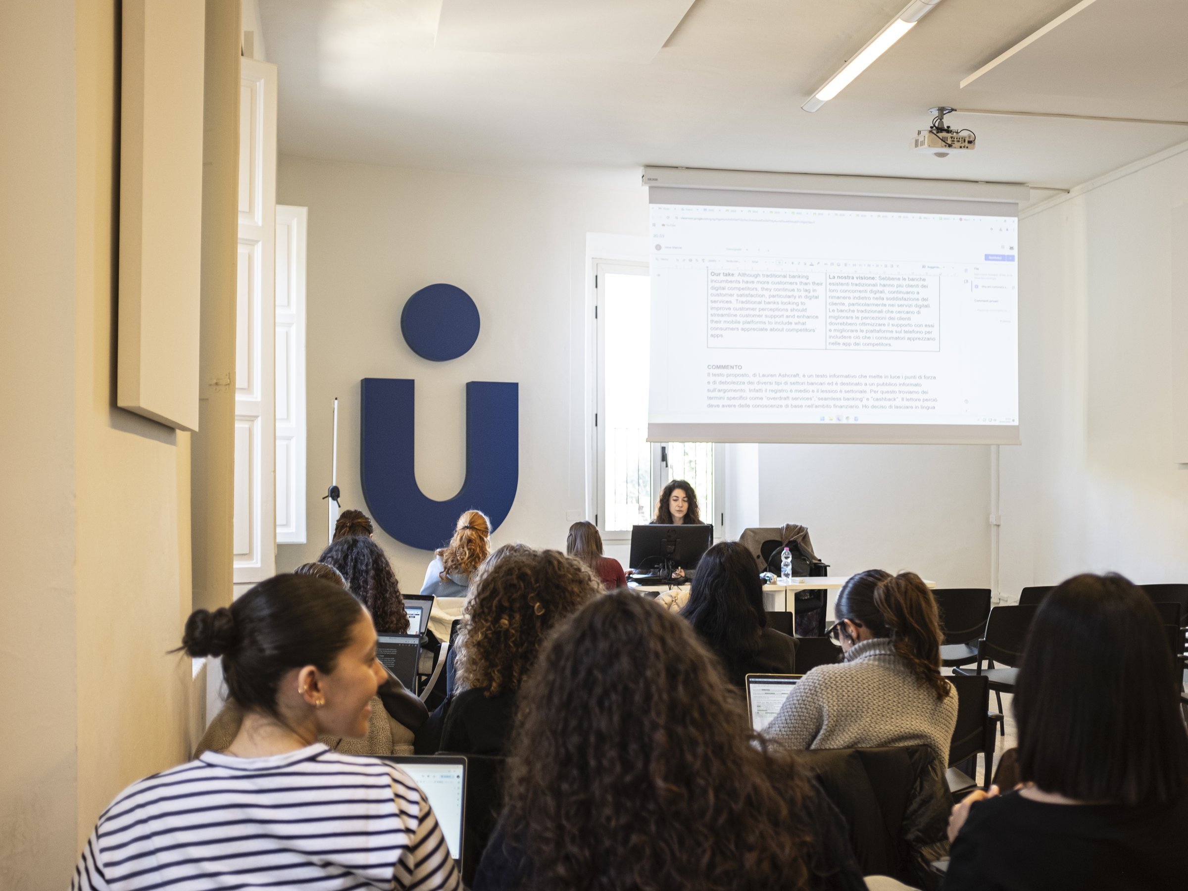 A visiting cohort at work in a Unicollege lecture room beneath the university mark
