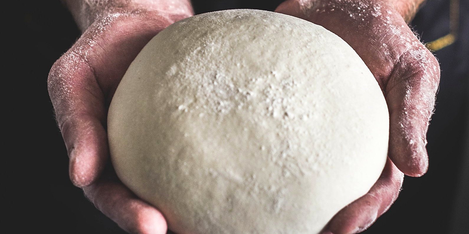 Floured hands shaping a ball of dough