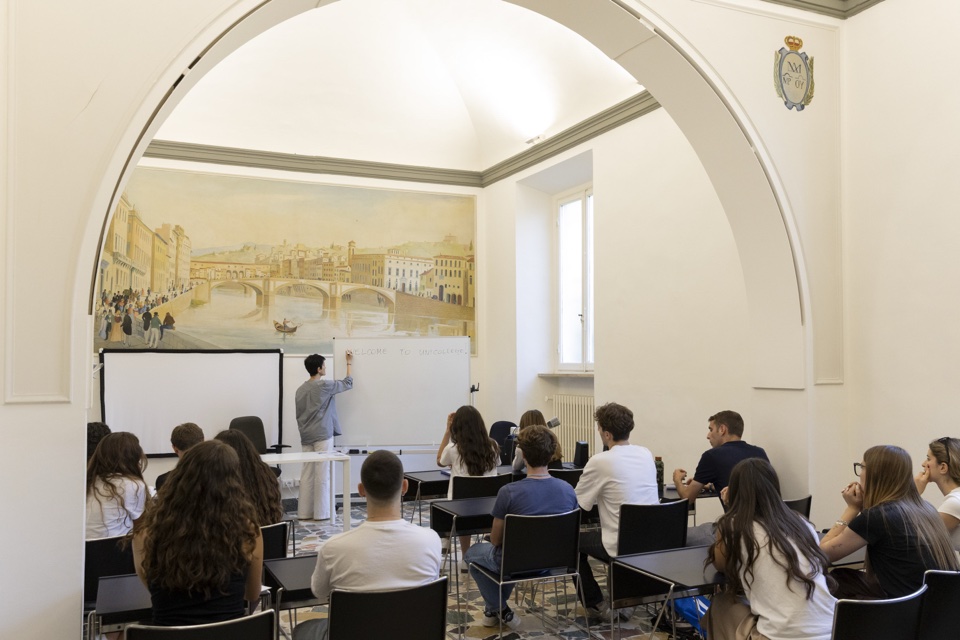 A lecture under the arch of the frescoed hall, with the Florence mural