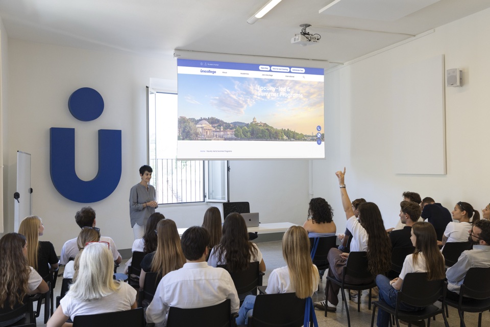 A lecture with the projector on and a student raising her hand
