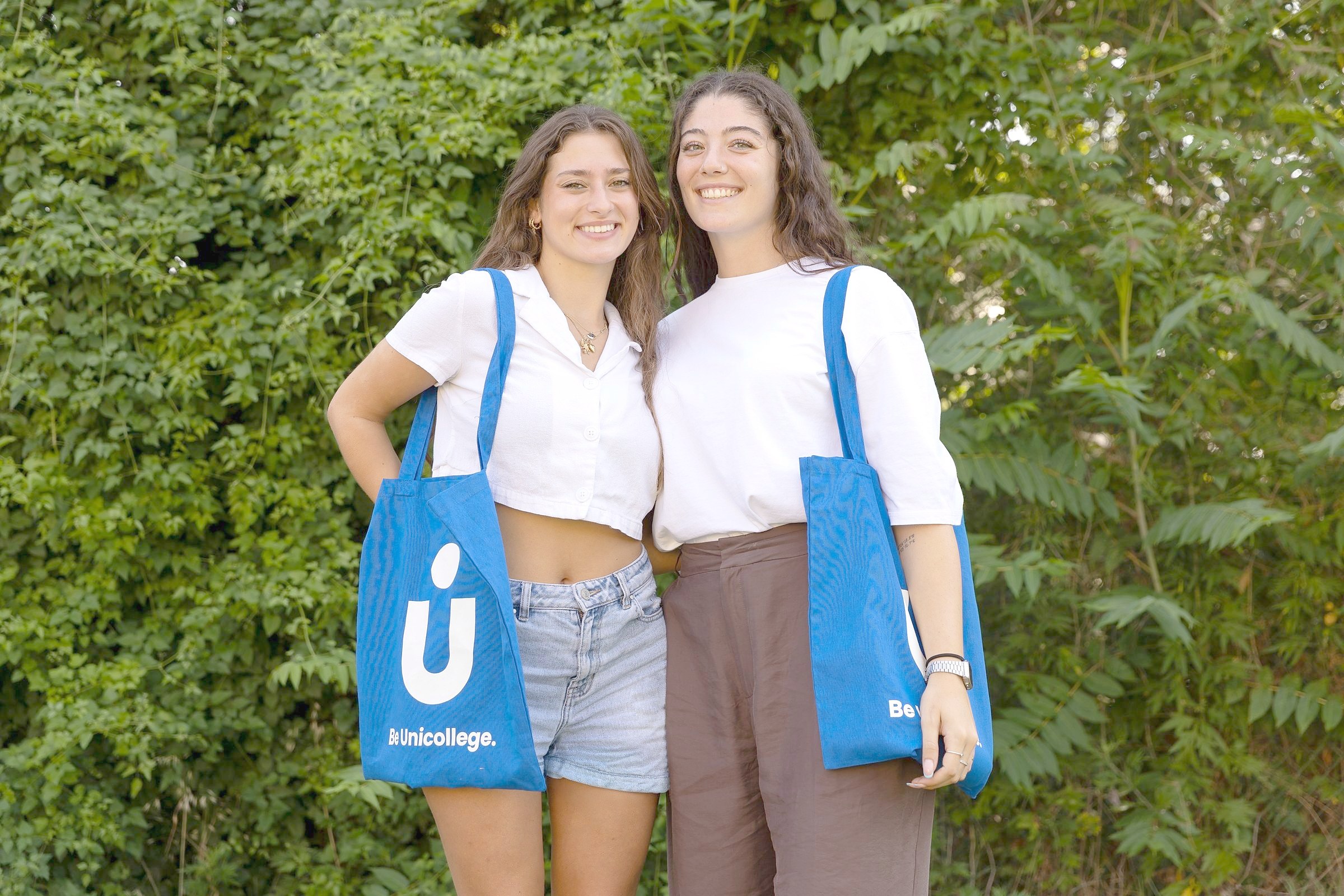 Two visiting students with Unicollege tote bags on the campus grounds