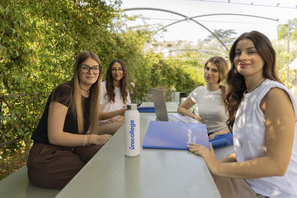 Four students at a garden table under the pergola, with a Unicollege bottle