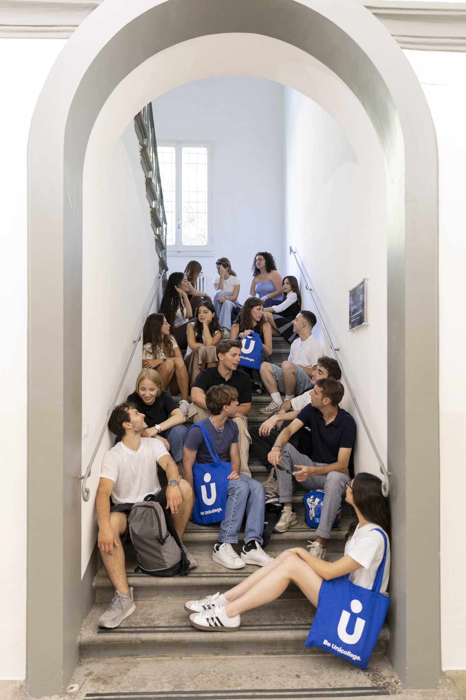 Students sitting on a campus staircase beneath an arched doorway