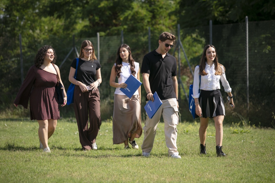 Five students walking across the campus lawn with their folders
