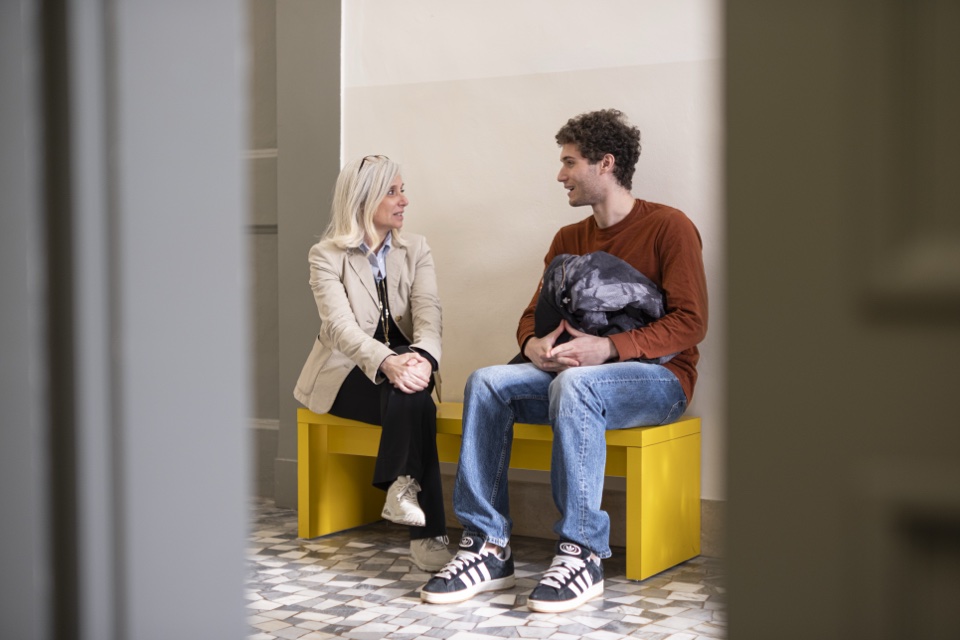 Two students in conversation on the yellow bench in the corridor